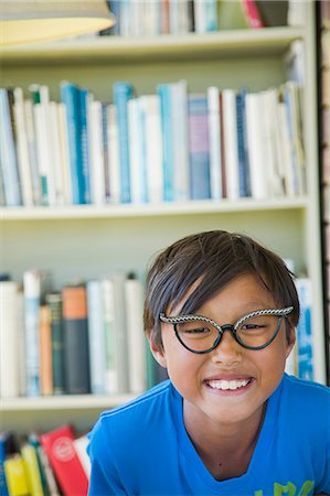 simsearch:673-08139172,k - Boy wearing vintage glasses smiles in front of a bookcase Stock Photo - Premium Royalty-Free, Code: 673-08139174