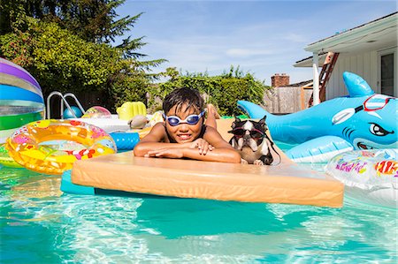 Boy and his Boston Terrier wearing matching goggles float on a toy in a pool Foto de stock - Sin royalties Premium, Código: 673-08139182