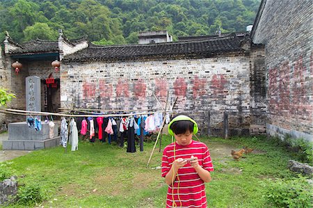 Boy wearing headphones uses an electronic device in a rural Chinese village Foto de stock - Sin royalties Premium, Código: 673-08139277