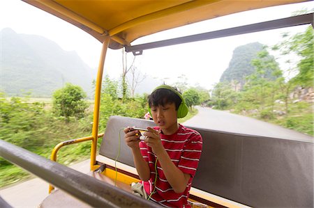 simsearch:673-08139279,k - Boy wearing headphones uses an electronic device while riding a village jitney Stock Photo - Premium Royalty-Free, Code: 673-08139280