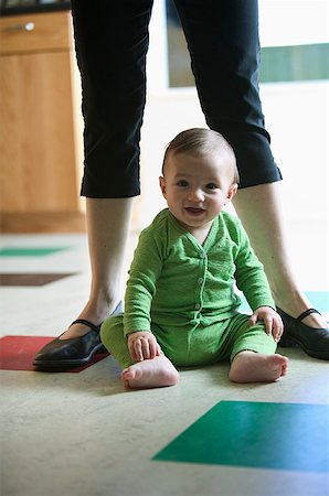 A baby sitting on kitchen floor with his mom behind him. Stock Photo - Premium Royalty-Free, Code: 673-02137593