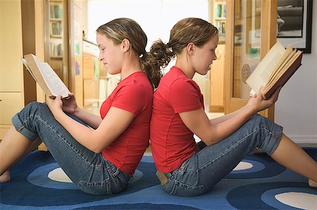 simsearch:673-02137877,k - Teenage twin girls sit back to back while reading. Foto de stock - Royalty Free Premium, Número: 673-02137742