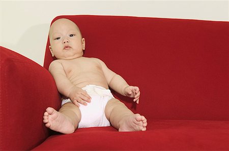 A baby seated on a red sofa and wearing a diaper. Stock Photo - Premium Royalty-Free, Code: 673-02138324