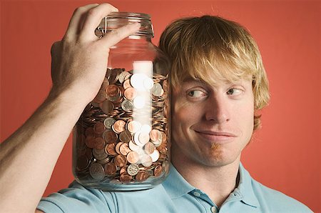 Young man eyeballing a large glass coin jar on his shoulder. Stock Photo - Premium Royalty-Free, Code: 673-02138610