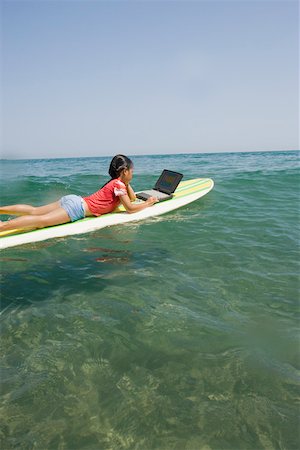 Petite fille à l'aide d'ordinateur portable sur une planche de surf Photographie de stock - Premium Libres de Droits, Code: 673-02140076
