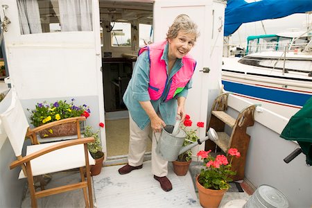 senior gardening looking at camera - Woman on houseboat watering plants Stock Photo - Premium Royalty-Free, Code: 673-02140621