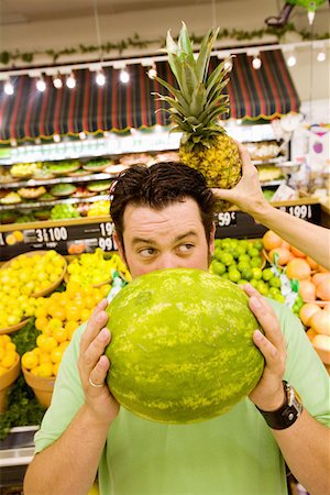 Man holding watermelon in supermarket as woman holds pineapple behind his head Fotografie stock - Premium Royalty-Free, Codice: 673-02141524