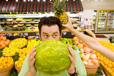 Man holding watermelon in supermarket as woman holds pineapple behind his head Fotografie stock - Premium Royalty-Free, Codice: 673-02141523