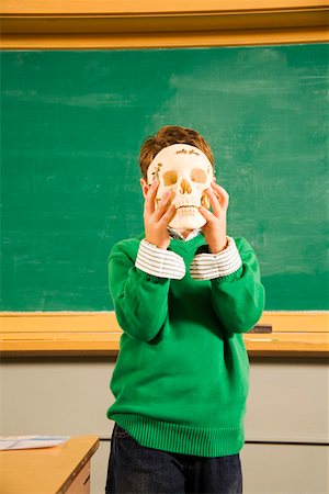 Boy holding Schädel über Gesicht im Klassenzimmer Stockbilder - Premium RF Lizenzfrei, Bildnummer: 673-02141867