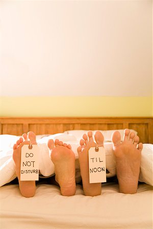 simsearch:673-02142131,k - Couple’s bare feet with Do Not Disturb Til Noon signs Stock Photo - Premium Royalty-Free, Code: 673-02142123