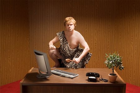 Businessman dressed as caveman crouching at desk Stock Photo - Premium Royalty-Free, Code: 673-02142145