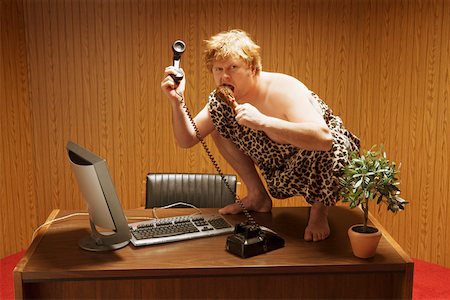 drumstick - Businessman dressed as caveman crouching on desk Stock Photo - Premium Royalty-Free, Code: 673-02142142