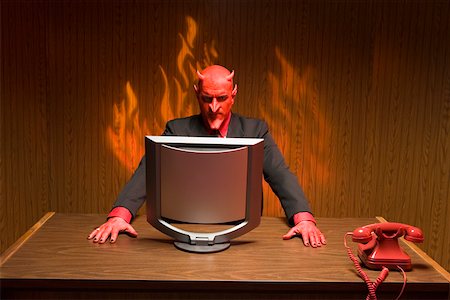 Businessman dressed as devil looking at computer Stock Photo - Premium Royalty-Free, Code: 673-02142172