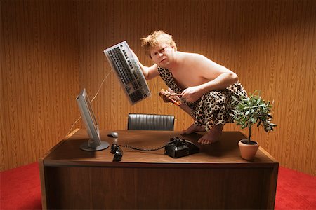 puzzled confused guy computer - Businessman dressed as caveman crouching on desk Stock Photo - Premium Royalty-Free, Code: 673-02142324
