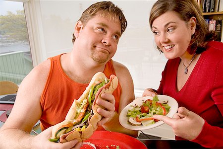 fat man food - Woman offering her husband a salad instead of sandwich Stock Photo - Premium Royalty-Free, Code: 673-02142401