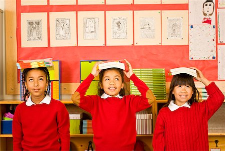 Multi-ethnic girl balancing school books on heads Stock Photo - Premium Royalty-Free, Code: 673-02143676