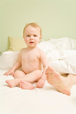 Curious baby sitting next to mother’s feet in bed Stock Photo - Premium Royalty-Free, Code: 673-02216290