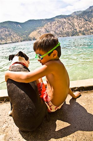 Boy sitting by lake with boston terrier dog Stock Photo - Premium Royalty-Free, Code: 673-03405744