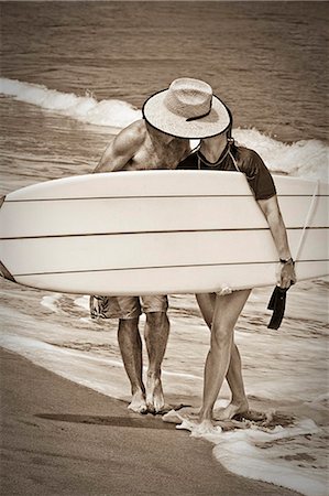 people walking in black and white - couple kissing behind surfboard Stock Photo - Premium Royalty-Free, Code: 673-03623191