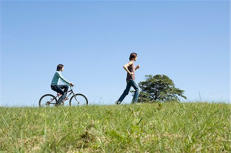 simsearch:685-02939247,k - Young woman riding bicycle behind young man running Stock Photo - Premium Royalty-Free, Code: 685-02939236
