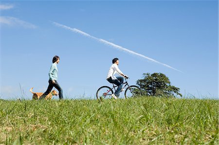 simsearch:685-02939244,k - Young woman walking dog behind young man riding bicycle Stock Photo - Premium Royalty-Free, Code: 685-02939237