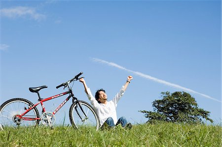 simsearch:685-02939247,k - Young man sitting next to bicycle, arms outstretched Foto de stock - Royalty Free Premium, Número: 685-02939241