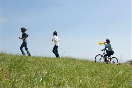 simsearch:685-02939247,k - Young woman riding bicycle behind two young men running Foto de stock - Royalty Free Premium, Número: 685-02939271
