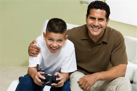 simsearch:694-03330729,k - Père avec fils jouer au jeu vidéo sur le canapé dans le salon, portrait Photographie de stock - Premium Libres de Droits, Code: 694-03318026
