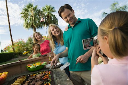 Daughter (7-9) video taping parents, grandmother, sister (7-9) at outdoor barbecue. Stock Photo - Premium Royalty-Free, Code: 694-03318107