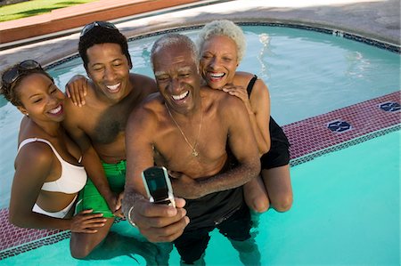 Senior couple and mid-adult couple posing for mobile phone photograph at swimming pool, elevated view. Stock Photo - Premium Royalty-Free, Code: 694-03318127