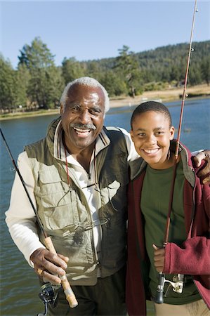 simsearch:694-03318999,k - Grandfather and grandson holding fishing rods by lake, smiling, (portrait) Fotografie stock - Premium Royalty-Free, Codice: 694-03318961