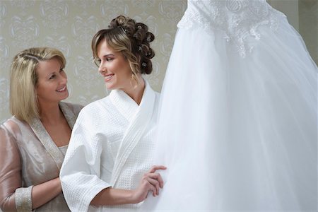 Bride in bathrobe touching wedding dress, mother looking on Foto de stock - Sin royalties Premium, Código: 694-03326805