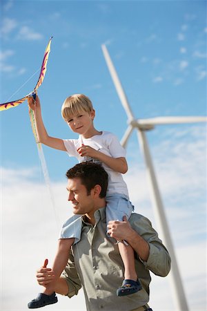 Boy (7-9) holding kite, sitting on fathers shoulders at wind farm Fotografie stock - Premium Royalty-Free, Codice: 694-03328222