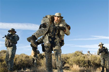 Soldiers walking in field, one carrying colleague Stock Photo - Premium Royalty-Free, Code: 694-03328346