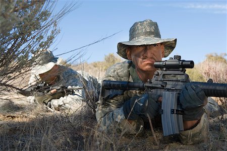 Soldiers aiming rifles in field, focus on soldier in foreground Stock Photo - Premium Royalty-Free, Code: 694-03328383