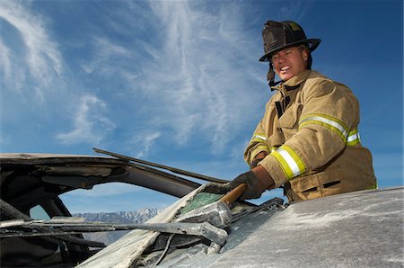 firemen uniform - Firefighter hitting crashed car with hammer Stock Photo - Premium Royalty-Free, Code: 694-03328494