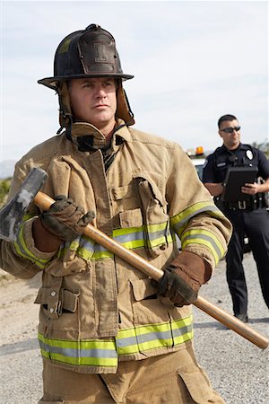 fireman portrait - Firefighter with axe, police officer in background Stock Photo - Premium Royalty-Free, Code: 694-03328535