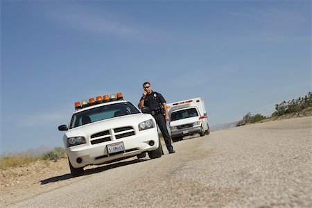 Police officer standing by police car with ambulance in background Stock Photo - Premium Royalty-Free, Code: 694-03328554