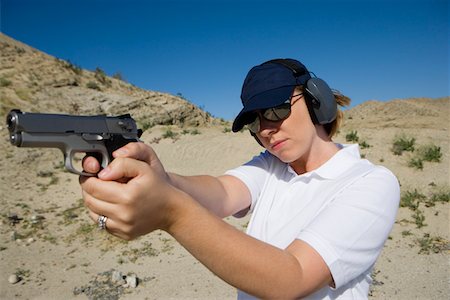 simsearch:694-03328595,k - Woman aiming hand gun at firing range in desert Fotografie stock - Premium Royalty-Free, Codice: 694-03328625