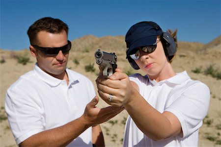 Instructor assisting woman aiming hand gun at firing range in desert Stock Photo - Premium Royalty-Free, Code: 694-03328623