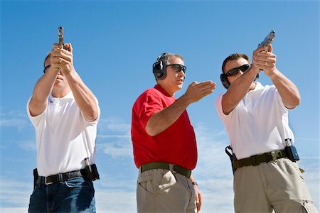 simsearch:694-03328608,k - Instructor assisting men aiming hand guns at firing range Foto de stock - Royalty Free Premium, Número: 694-03328637