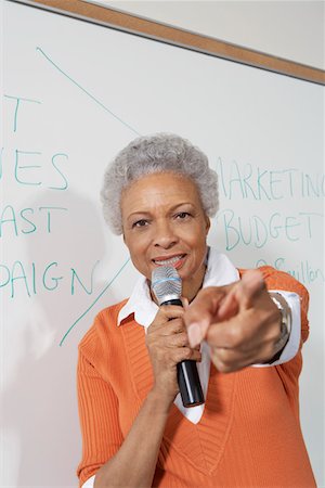 Female teacher using microphone, pointing near white board Stock Photo - Premium Royalty-Free, Code: 694-03328973