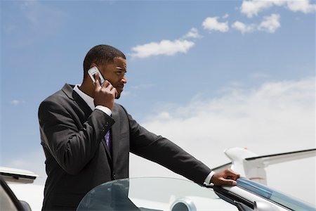 Mid-adult businessman standing in convertible and using mobile phone. Stock Photo - Premium Royalty-Free, Code: 694-03322092
