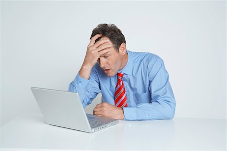 Studio shot of businessman with head in hands using laptop Stock Photo - Premium Royalty-Free, Code: 694-03331798