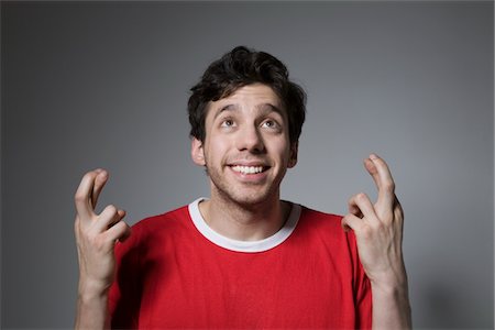 quirky person 20s - Young man in red top looking up with fingers crossed Stock Photo - Premium Royalty-Free, Code: 694-03333063