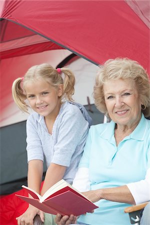 simsearch:400-03923096,k - Grandmother sits reading a book with her grand-daughter outside a tent Stock Photo - Premium Royalty-Free, Code: 694-03440960