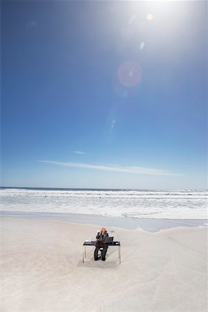Senior business man sitting at office desk on beach, elevated view Stock Photo - Premium Royalty-Free, Code: 694-03694064