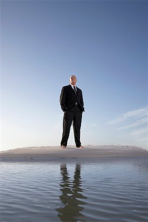 Business man standing on beach, portrait, low angle view Foto de stock - Royalty Free Premium, Número: 694-03694065