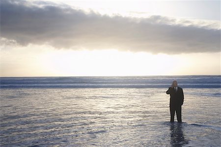 Business man using mobile phone standing in sea at sunset, elevated view Stock Photo - Premium Royalty-Free, Code: 694-03694066