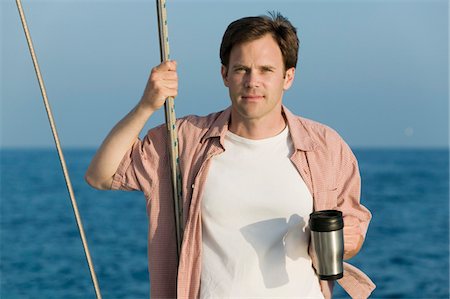 Man standing on sailboat, holding coffee mug, (portrait) Stock Photo - Premium Royalty-Free, Code: 694-03692819